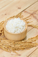 bowl full of rice and ear of rice on wooden background