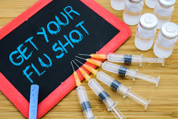 Get Your Flu shot written on chalkboard with vaccine in syringes