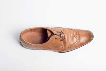A worn brown mans oxford brogue shoe isolated on a white background.