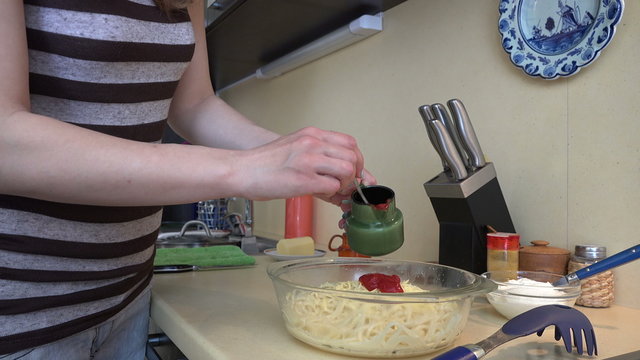 Female hands put red sauce on spaghetti pasta in dish. Preparing vegetarian food. Static closeup shot. 4K UHD video clip.