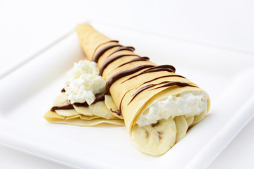 Crepe stuffed with banana and whipped cream decorated with chocolate syrup