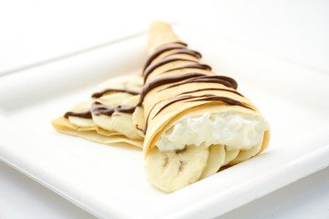 Crepe stuffed with banana and whipped cream decorated with chocolate syrup
