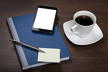 Top view on dark wooden office desk with notepad, pen, sticky note, mobile with blank screen and cup of coffee.