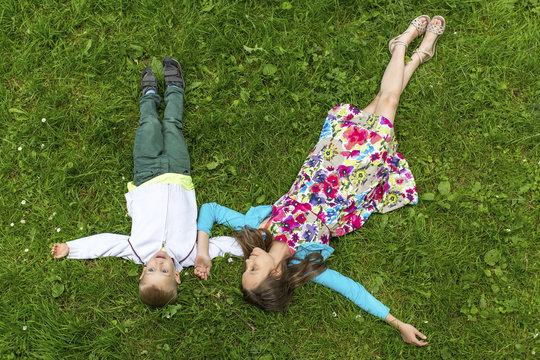 Cute girl with her little brother lying on the green grass, top view.