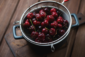 Colander with fresh sweet cherries on a dark wooden background