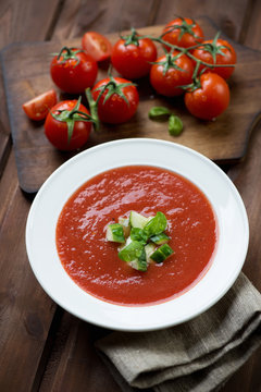 Glass plate with tomato soup gazpacho, dark wooden background
