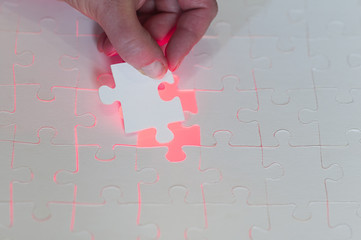 Hand setzt letztes Puzzleteil ein/Symbol fuer Loesungen von Geschaeftskonzepten, Hand setzt letztes Puzzleteil ein mit rotem leuchtendem Hintergrund.