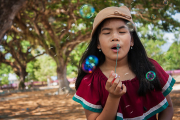 Little asian cute girl playing with bubble wand blowing soap bubbles in the garden background