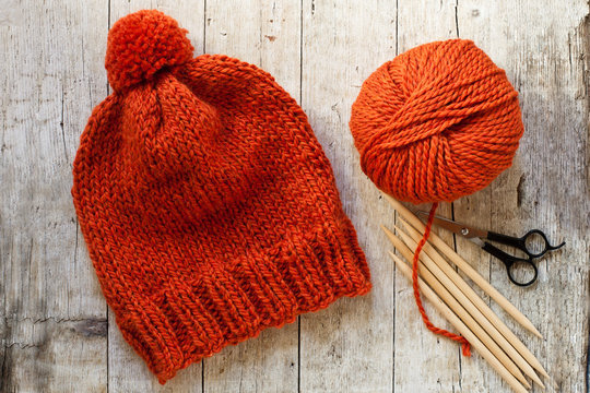 wool orange hat, knitting needles and yarn