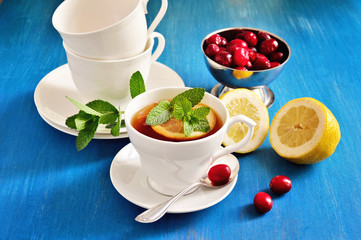 Tea with lemon, mint, and fresh cranberries on a blue background. Selective focus