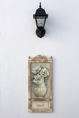 Street lamp and wooden ornament hanged on white wall of an old hotel in Bozcaada