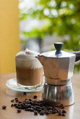 a moka pot and a cup of coffee with roasted coffee beans