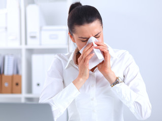 Young businesswoman blowing her nose, sits at the desk