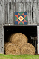 Vertical-wooden barn with quilt block, filled with hay bales.