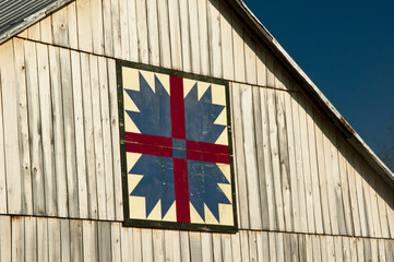 Beautiful wooden barn with blue/red quilt pattern decoration against a blue sky. © bettys4240
