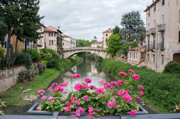 Fototapeta na wymiar Flowered balcony of Saint Paul bridge in Vicenza, Retrone river and Saint Michele bridge in the background
