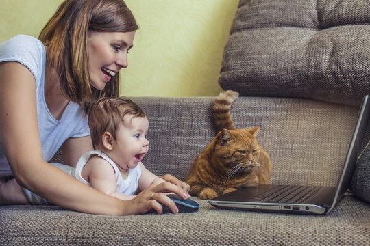 Woman With A Baby And A Cat At The Laptop Lying On The Couch