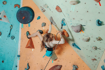 Girl in safety equipment climbing in gym