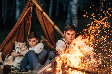 Obraz na płótnie Canvas two twin brothers sitting around a campfire in a birch grove