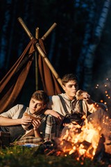 two twin brothers sitting around a campfire in a birch grove