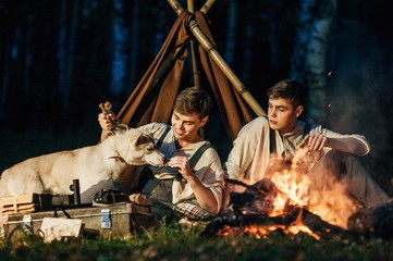Fototapeta na wymiar two twin brothers sitting around a campfire in a birch grove