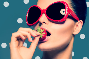 Sexy woman in big red sunglasses eating strawberry