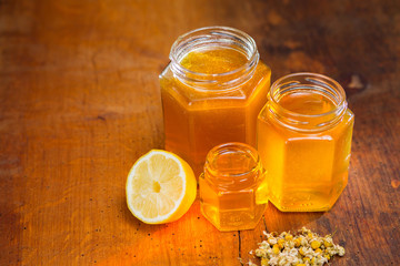 honey in a glass with label on a wooden table with chamomile tea and lemon
