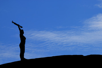 Silhouette of woman lifting tripod under the blue sky.