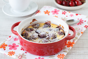 Clafoutis with cherries in red ramekin on wooden background