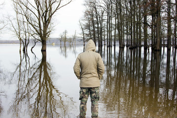 Fototapeta na wymiar Man in jacket and military pants standing on shore and observing river