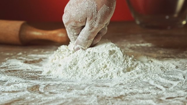 Baker hand preparing flour on the table to make dough, slow motion, 240 fps. Cooking and backing preparation. Food preparation on the red kitchen background.