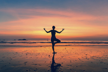 Silhouette of woman standing at yoga pose on the beach during fantastic sunset.