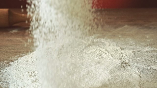 Sifting flour through sieve, slow motion 240fps. Baker sifting measured flour on a table. Cooking and backing preparation. Food preparation on the red kitchen background.