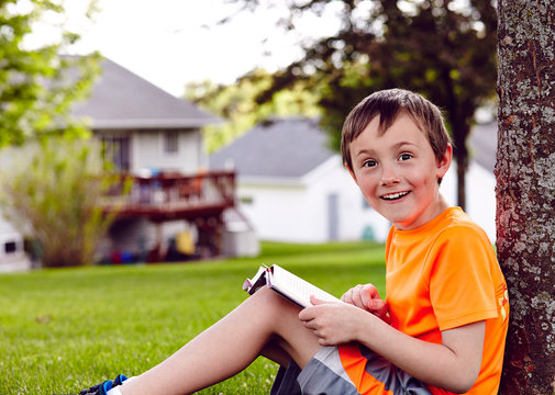 Handsome  boy reading a book on a lawn near house 