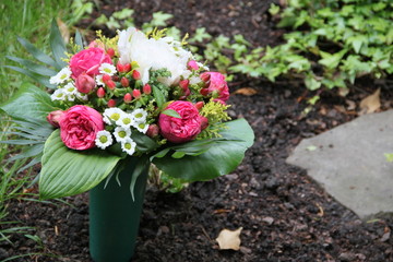 Bunte Blumen in Friedhofsvase schmücken ein Grab