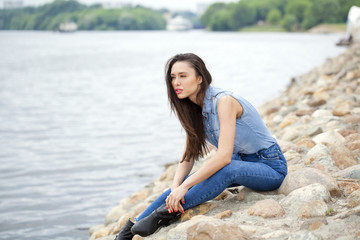 Fototapeta na wymiar Young beautiful brunette girl sitting on the rocks on the river