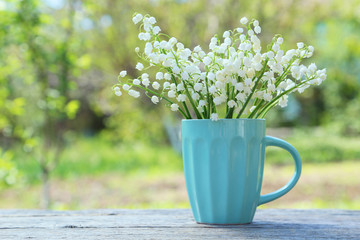 Lily of the Valley in cup on grey wooden background, outdoors