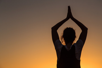 Silhouette young woman practicing yoga on the beach at sunset.