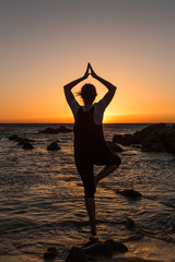 Silhouette young woman practicing yoga on the beach at sunset.