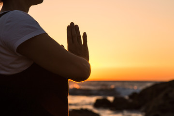 Silhouette young woman practicing yoga on the beach at sunset.