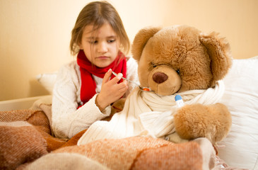 girl playing and measuring teddy's bear temperature with thermom