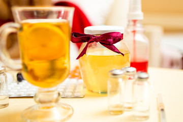 Closeup of hot tea, honey jar and pills on bedside table