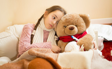 sick girl resting in bed with brown teddy bear