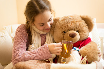Closeup of little sick girl giving hot tea to teddy bear