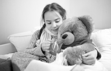 portrait of cute girl lying in bed and giving pills to teddy bea