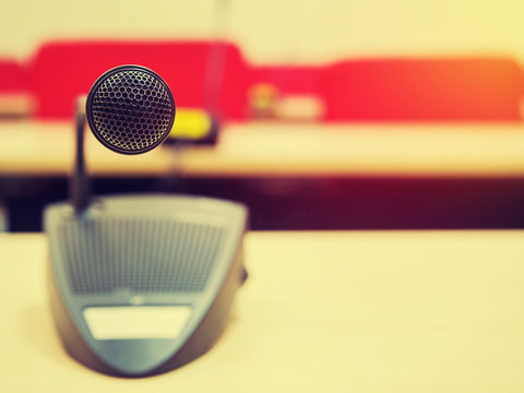 Vintage style photo of the microphone in conference room or symposium event with de focused meeting room in background. Extremely shallow dof. Filtered process.