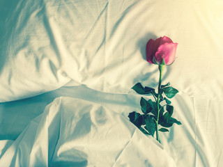 Fototapeta premium Vintage styled image of a romantic getaway with red roses on fluffy pillows and bed. For love concept or background.