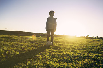 Portrait of a boy staying on green grass with soccer ball 