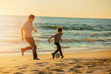 Happy father and son play soccer or football on the beach in
