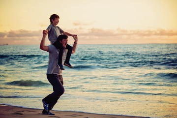 Happy father and son having great time on the beach in sunset